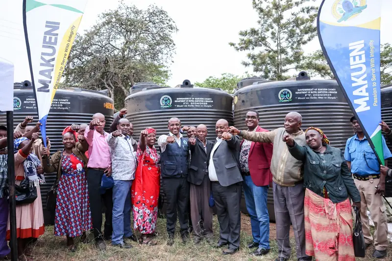 Mutula Kilonzo Jr. with community representatives beside newly distributed water tanks.